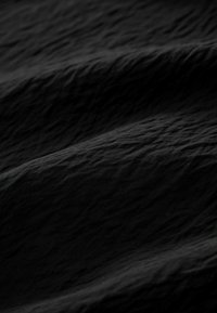 Tessuto nero dalle texture con pieghe ondulate, caratterizzato da una superficie leggermente stropicciata che riflette la luce in modo morbido.