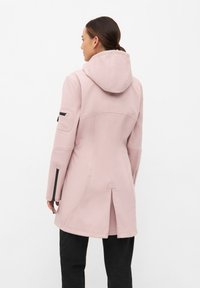 Chaqueta con capucha de un suave material color rosa claro, que presenta cremalleras laterales, una abertura en la parte trasera y costuras curvadas que le otorgan un diseño estructurado.