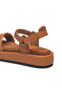 Tan leather platform sandals with a padded suede footbed, adjustable straps, and a thick sole featuring a textured black bottom.