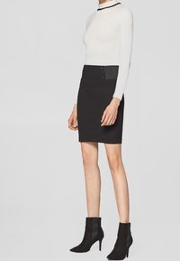 Bílý dlouhý rukáv top s přiléhavým střihem. Černá tužková sukně s vysokým pasem, se strukturovaným páskem a třemi dekorativními knoflíky. Černé kotníkové boty.