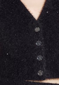 Cardigan noir duveteux avec des boutons argentés brillants et de subtils accents pailletés, présentant une coupe courte et une encolure en V.