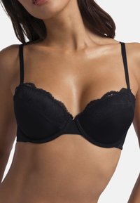 Soutien-gorge noir avec bordures en dentelle, à coques moulées et bretelles réglables. Texture de tissu lisse et motif floral délicat sur la dentelle.