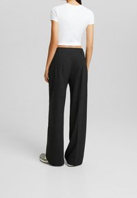 Svarta vida byxor i tyg med en slät textur, med en midje med medelhög höjd och rena bakfickor. Minimalistisk design.