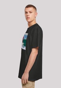 Camiseta de algodón negra con un estampado gráfico de un surfista en una ola. Mangas cortas y corte relajado; textura suave.