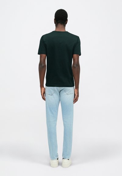 Μαύρη βαμβακερή μπλούζα εμφανιζόμενη από πίσω, συνδυασμένη με ανοιχτό μπλε τζιν παν�τελόνι. Τα αθλητικά παπούτσια είναι μπεζ με λεπτομέρεια στη σόλα.