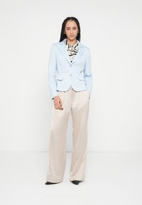 Blazer azul claro con dos bolsillos delanteros y un solo botón. Debajo, una blusa a rayas en blanco y negro. Pantalones de pierna ancha color crema con tacones.