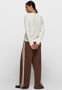 Haut crème à manches longues avec un col rond, associé à un pantalon large marron avec des bandes latérales. Tissu doux et coupe décontractée.