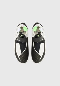 Black and white climbing shoes with a mesh upper, rubber sole, velcro strap, and green accents at the heel and tongue.
