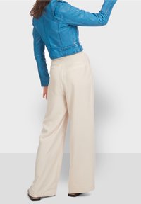 Chaqueta de cuero azul corta con una cintura entallada y mangas largas, combinada con pantalones crema de pernera ancha. Textura suave y detalles mínimos.