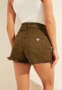 Zielone oliwkowe szorty dżinsowe z postrzępionym dołem, z wysokim stanem i dwoma tylnymi kieszeniami. Na prawej kieszeni znajduje się trójkątna naszywka z logo.