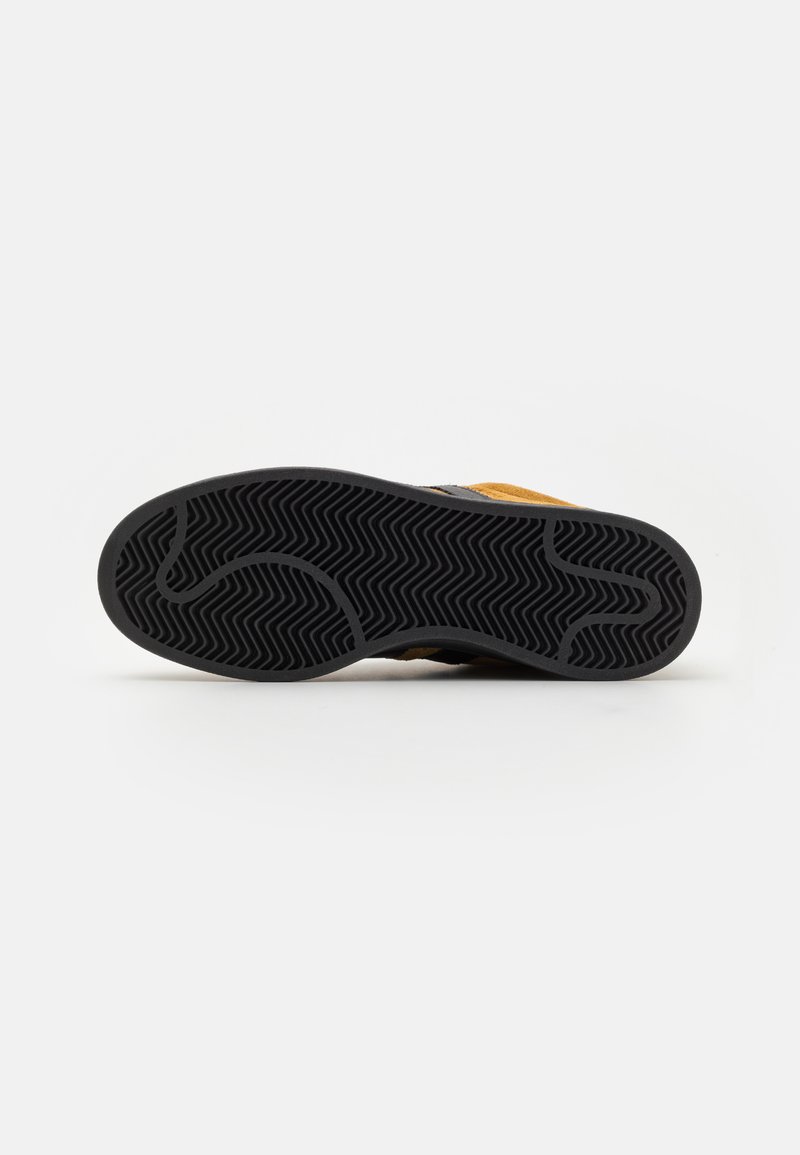 Suela de goma negra con patrón en zigzag, con parte superior de ante marrón y acentos en negro. El diseño es elegante y minimalista.