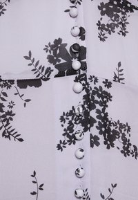 Gros plan d’un tissu avec un motif floral noir et une rangée verticale de boutons recouverts de tissu assortis au motif.