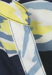 Gemusterter Stoff mit blauen, gelben und weißen abstrakten Blumenmustern; zeichnet sich durch kontrastierende Nähte entlang der Kanten aus.