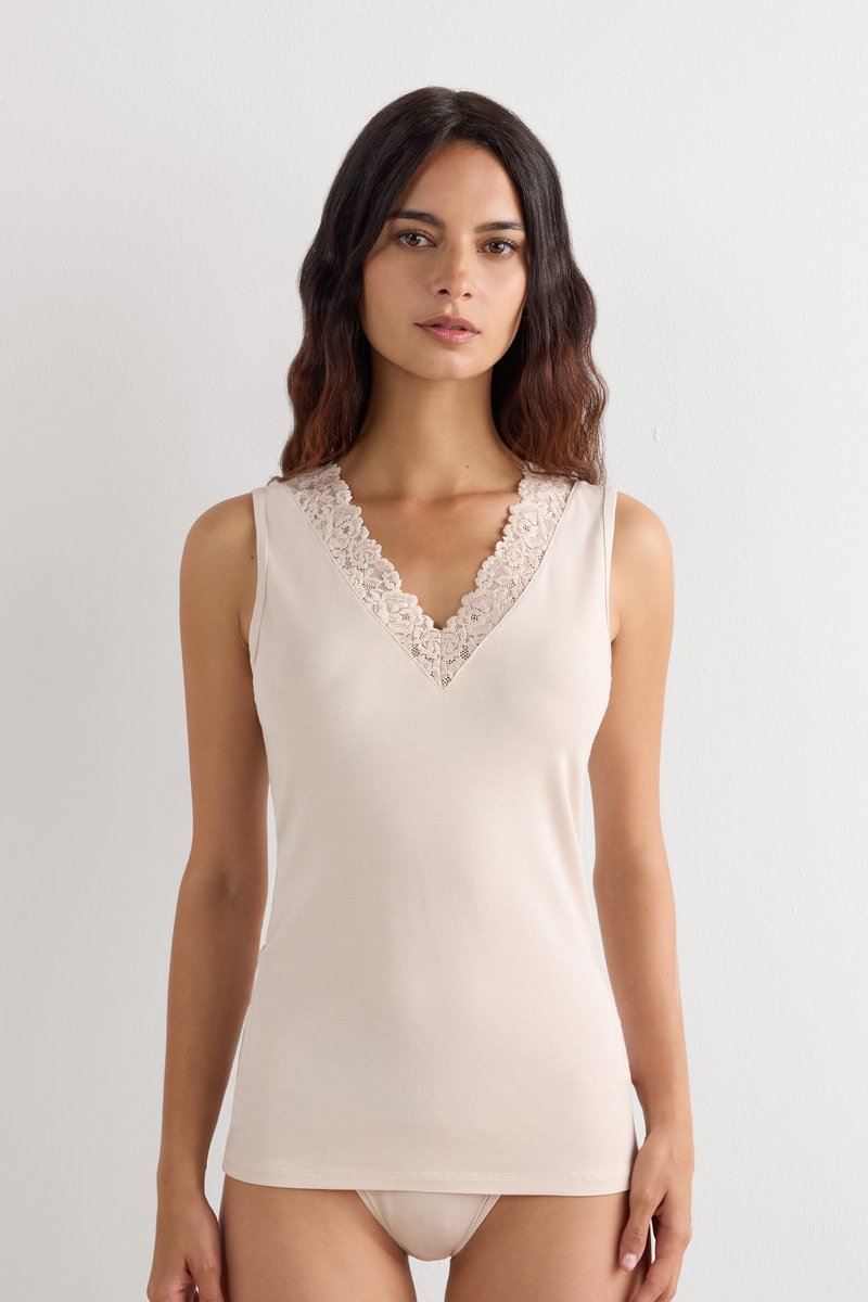 Vrouw met lang donker haar die een beige mouwloos top draagt met kanten afwerking aan de V-hals en bijpassend beige ondergoed.