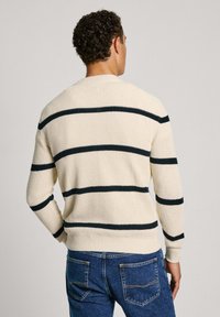 Maglione a maglia color crema con strisce orizzontali nere, caratterizzato da un motivo testurizzato e polsini e orlo a costine. Indossato con jeans in denim blu.