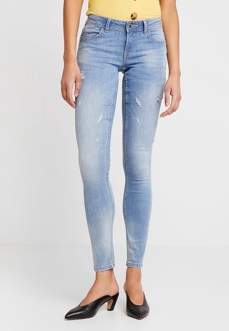 Ljust blå skinny jeans i denim, med en sliten design och subtila revärer, kombinerade med svarta spetsiga klackskor.