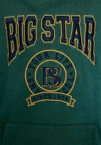 Maglione verde scuro con testo ricamato "BIG STAR" e logo circolare con "YOUR LIFE", accentuato in giallo e blu navy. Tasca frontale inclusa.