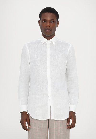 Chemise en lin blanc à manches longues, patte de boutonnage sur le devant et col classique. Texture lisse et coupe droite, associée à un pantalon à carreaux.