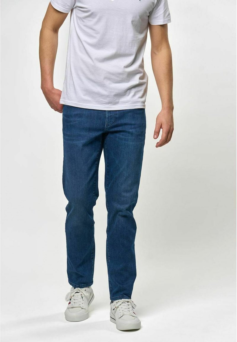 Modre jeans hlače z ozkim krojem, v kombinaciji z enostavno belo majico in belimi supergami. Gladka tekstura, osnovna zasnova in sproščen slog.