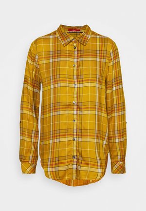 Camisa de manga larga a cuadros en color mostaza con cierre de botones en el frente y cuello puntiagudo, con líneas blancas, rojas y negras en el patrón.