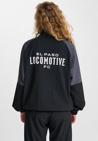 Svart sportjacka med grå ärmar, med "EL PASO LOCOMOTIVE FC" i vit text på baksidan. Mjuk tyg med elastiska ärmslut.