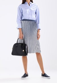 Czarna torebka ze wzorem węża krokodyla z zamkiem błyskawicznym i złotymi akcentami, zestawiona z jasnoniebieską koszulą w paski z guzikami oraz spódnicą w paski.