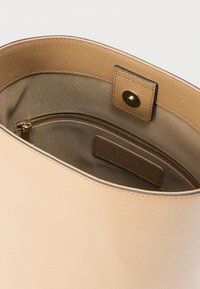 Beežist nahast käekott tekstuurse välimusega, millel on avar beež sisemus ja tõmblukuga tasku organiseerimiseks.