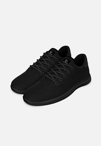 Chaussures de sport noires avec tige en mesh, lacets plats, bout arrondi et semelle texturée. Design minimaliste avec amorti au niveau du col.