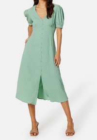 Mintgrön midi-klänning i texturerat tyg, puffärm, V-ringning, knäppning fram och en framtill slits. Flata sandaler kompletterar looken.