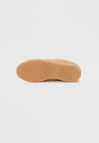 Tan sneakersåle med et mønstret gummisåle, som har hexagonale og cirkulære teksturer for godt grep og friksjon.