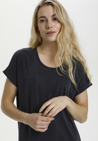 T-shirt corto a maniche corte di un blu navy scuro con scollatura rotonda. Texture morbida, vestibilità rilassata, polsini delle maniche piegati e superficie del tessuto liscia.