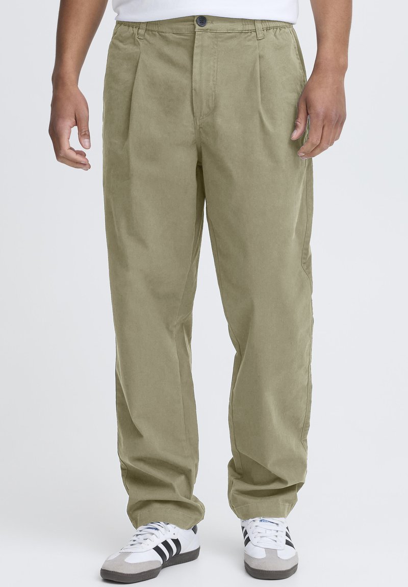 Pantalon plissé kaki en tissu doux et texturé ; il présente une taille à bouton, des poches latérales, et une coupe droite décontractée.