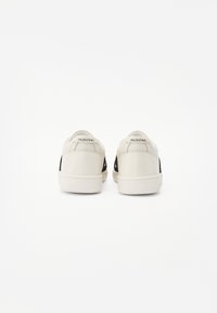Sneaker in pelle con una combinazione di colori bianco e nero. Presenta un design sobrio e suole in gomma piane, con il marchio "VALENTINO" sul tallone.