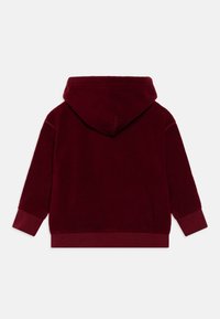 Haut à capuche en polaire bordeaux avec une capuche spacieuse, des poignets et un ourlet côtelés, doté d'une texture douce et sans motifs visibles.