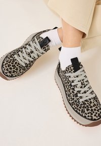 Sneaker con stampa leopardata, lacci grigi, dettagli neri sul tallone e suola in gomma marrone chiaro. Presenta una tomaia testurizzata e un design imbottito.