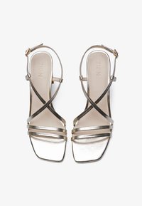 Gold metallic strappy sandals with a square toe design, featuring crossed ankle straps and a smooth finish on the sole.