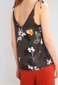 Czarna tank top w ciemnym florystycznym wzorze, z plecami w kształcie V, regulowanymi ramiączkami i jedwabistą fakturą, udekorowany pomarańczowymi i białymi kwiatami na czarnym tle.