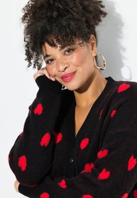 Schwarze Strickjacke mit roten Herzmustern, strukturiertem Stoff und V-Ausschnitt. Mit gerippten Bündchen und Knopfverschluss.