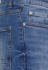 Jeans in denim con lavaggio blu, caratterizzati da differenti cuciture arancioni, rivetti in metallo e un classico design a cinque tasche.