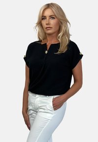 Czarny top z krótkim rękawem w serek, ozdobiony guzikami na rękawach, w połączeniu z białymi dopasowanymi spodniami o gładkiej fakturze.