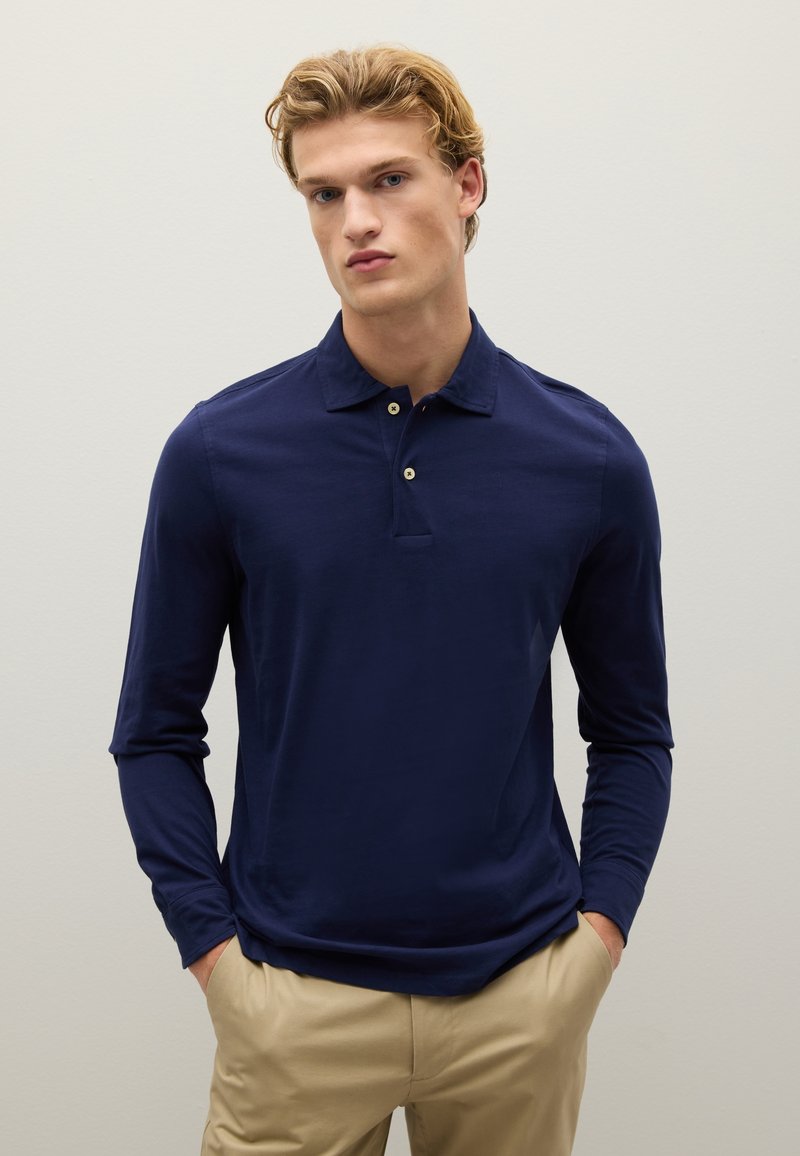 Navy poloshirt met lange mouwen, een zachte textuur, een sluiting met drie knopen en subtiele stiksels, gecombineerd met lichtgekleurde broeken.