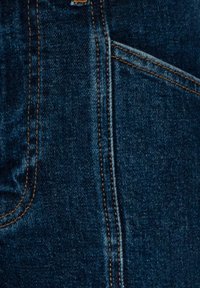 Gros plan sur un tissu en denim bleu foncé avec des surpiqûres orange et une couture visible de la poche avant.