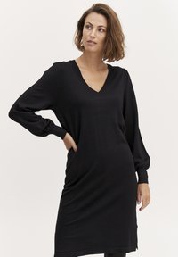 Vestito nero in maglia con scollatura a V, maniche lunghe e tasche laterali. Caratterizzato da una vestibilità comoda con polsini e orlo a coste. Texture liscia.