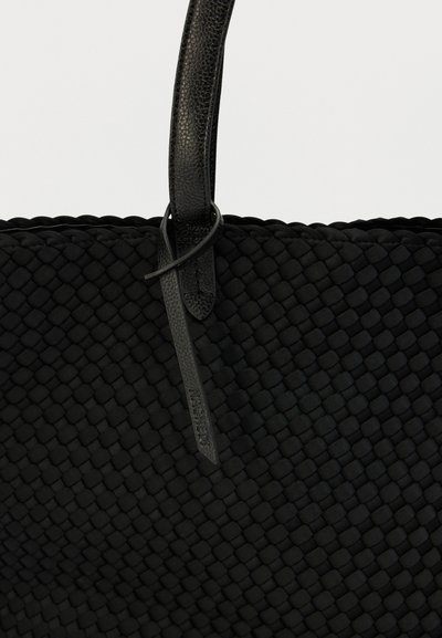 Μαύρη υφαντή τσάντα ώμου με υφή στην επιφάνεια. Λεπτές λαβές από λείο δέρμα και ετικέτα που αναγράφει το εμπορικό σήμα. Απλός, λειτουργικός σχεδιασμός.