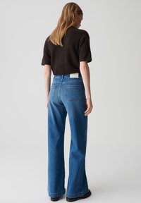 Blaue weit geschnittene Jeans mit hoher Taille und zwei Gesäßtaschen. Kombiniert mit einem dunklen, strukturierten Kurzarmpullover.