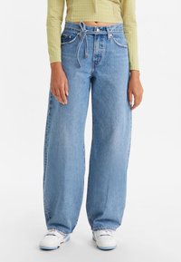 Ljust blå vida jeans i denim, med hög midja, snörning och trasig fåll, i kombination med vita sneakers.