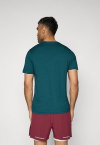 Teal bomulds T-shirt med korte �ærmer og rund hals, der har en glat struktur. Båret med bordeaux shorts, der viser hvid tekst.