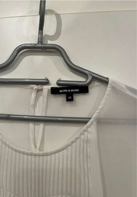 Vit blus med plisserad textur, rund halsringning och nyckelhålsdetalj på baksidan. Lappen visar "MORE & MORE" med storlek 40. Hänger på en grå galge.