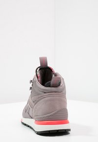 Grauer High-Top-Sneaker aus strukturiertem Stoff und Leder, akzentuiert mit einem roten Streifen an der Sohle und einem blumigen Futter, das innen am Kragen sichtbar ist.