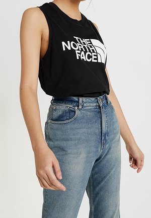 Black sleeveless cropped shirt with "THE NORTH FACE" logo in white, paired with high-waisted blue denim jeans with a faded finish.